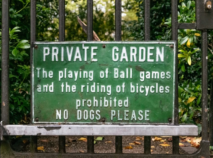 a green sign on black iron gate telling people to play the games