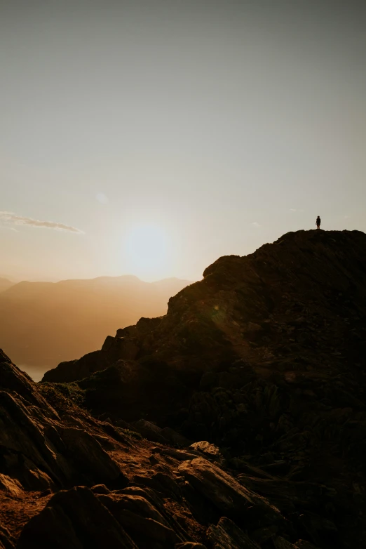 the sun sets behind a mountain with a man on top