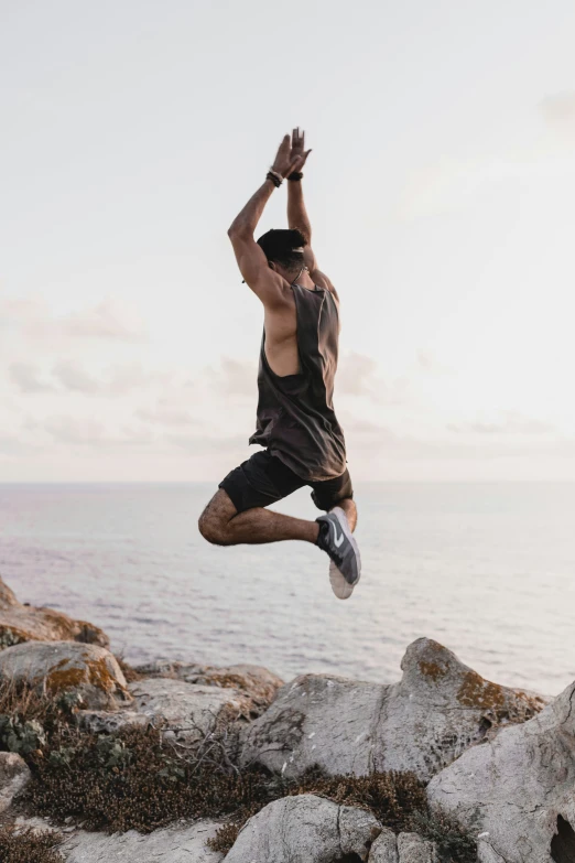 a man jumping in the air above a rocky shoreline