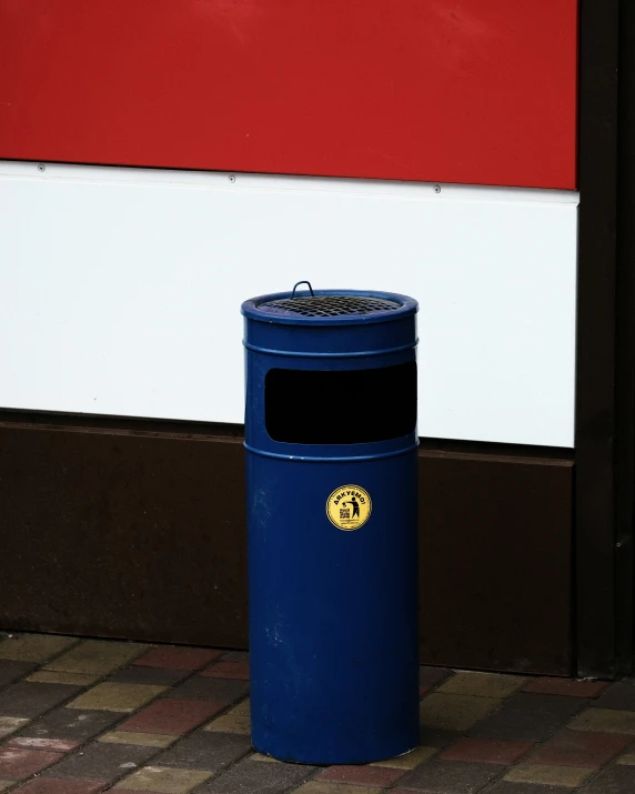 a blue trash can sitting on a tiled walkway