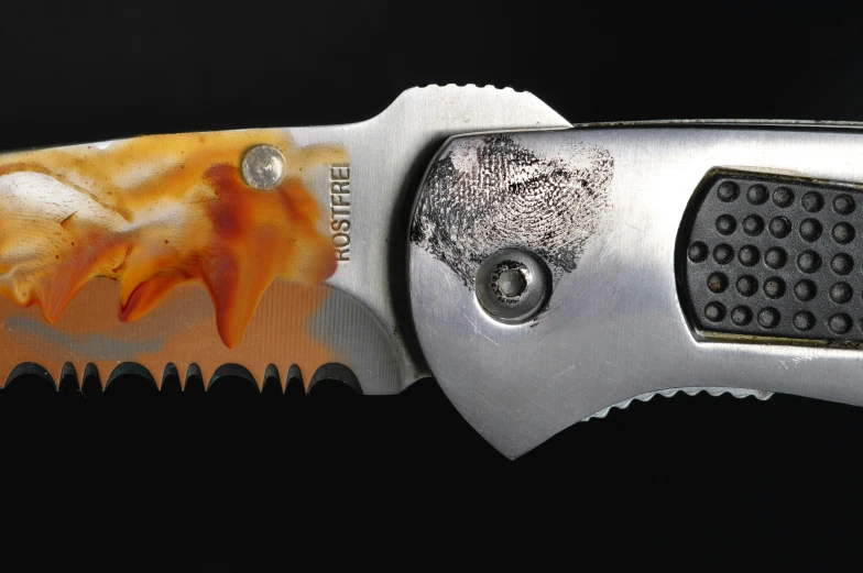 a close up of a knife with orange and white design on the blade