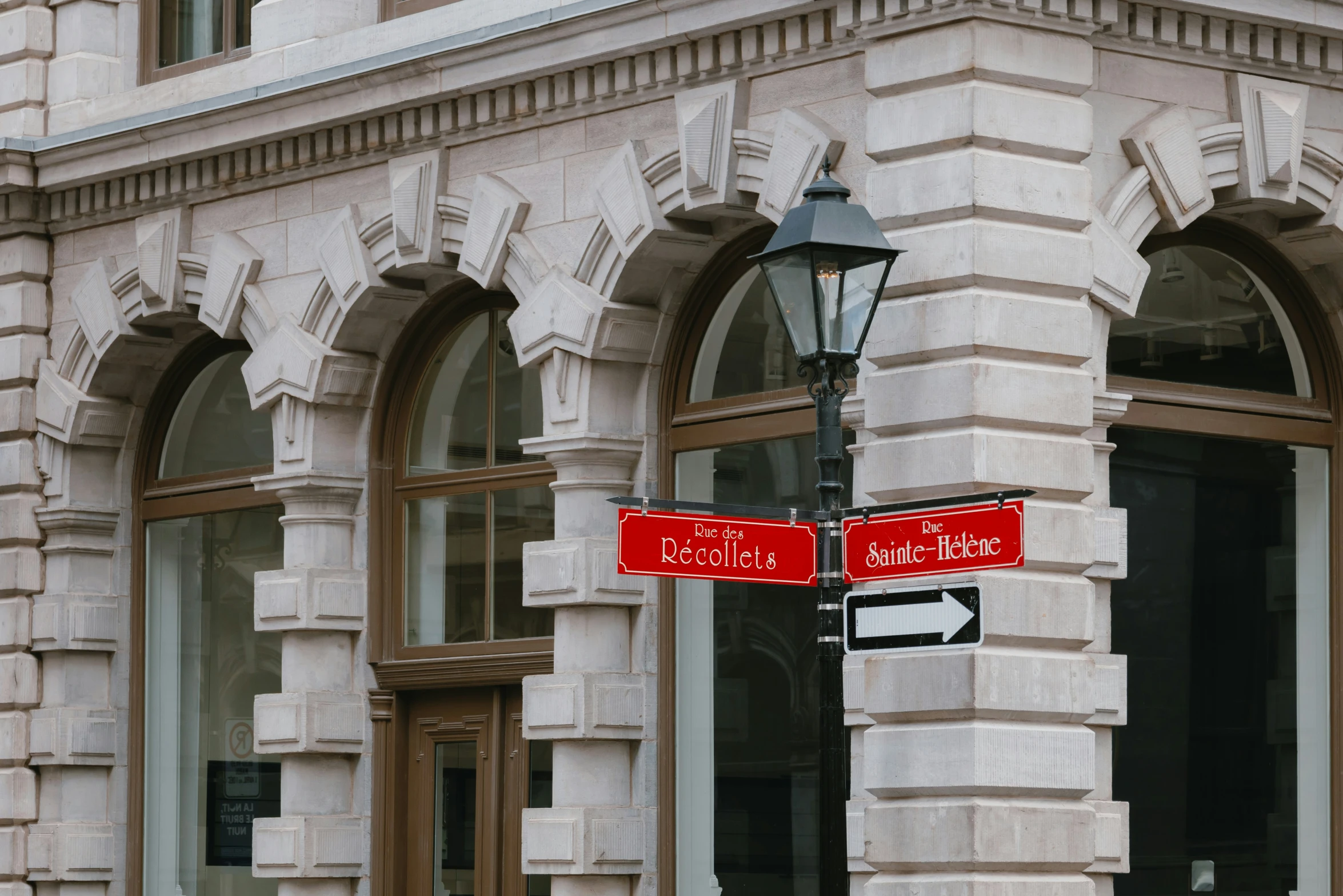 two red street signs on a lamp post next to windows