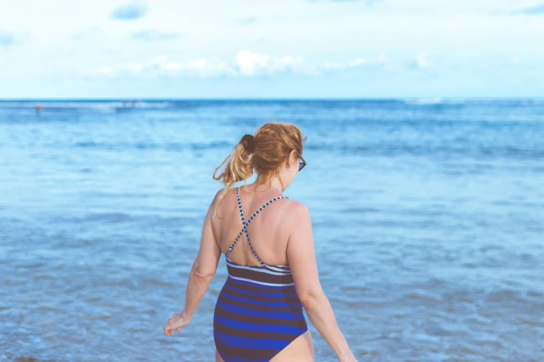 a woman in a one - piece swim suit is walking on the beach