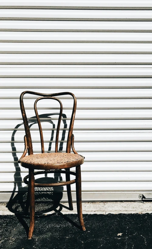 a bent back chair with wicker seat sitting against a white wall