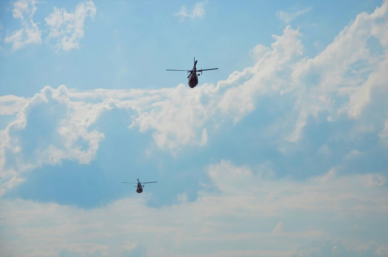 two military helicopters flying above the clouds during a sunny day