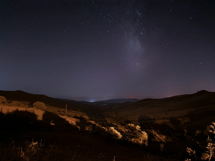 a night sky view with bright stars above a hilly valley