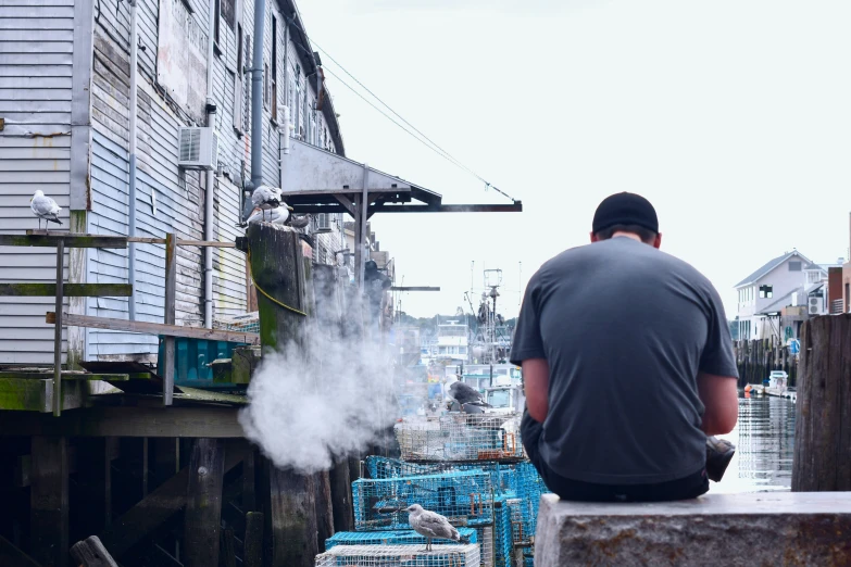 man sitting on a dock watching some type of steam rising from the river