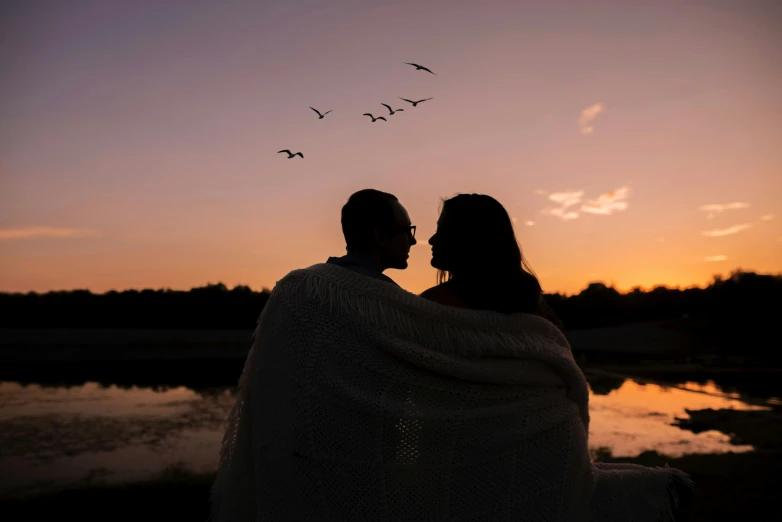 two people sit together on the shore of a lake