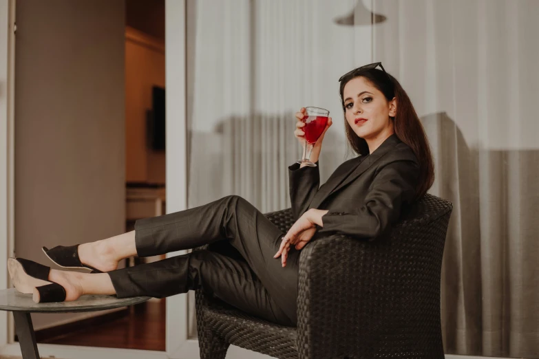 a woman is sitting with her legs crossed, holding up a glass with liquid