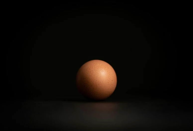 an egg sitting on a dark surface with a dark background