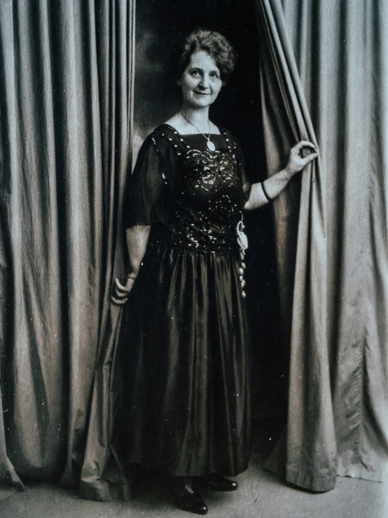 an old po of a woman standing in front of a curtain