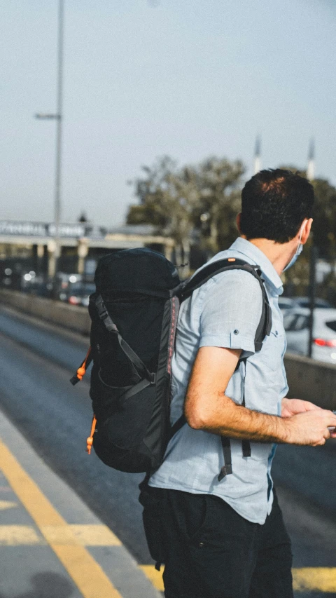 a young man with a black back pack waits on the side of the road