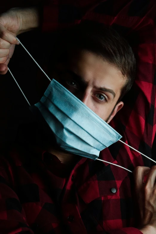 a man in plaid shirt and mask holding thread