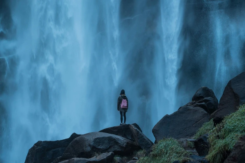 a man standing on a rock looking at a waterfall