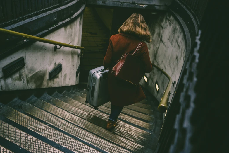 woman carrying a suitcase up an escalator that's going down