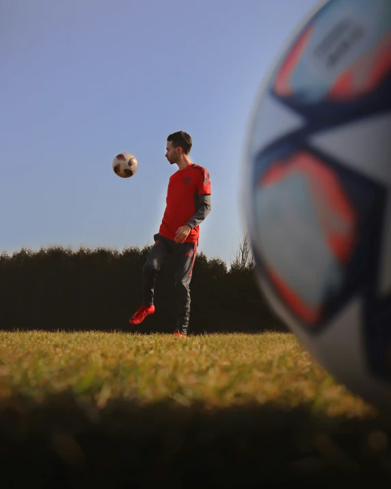 a young man wearing a red shirt is kicking a soccer ball in a field