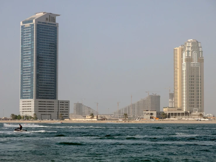 the boat is on the water in front of a beach with high buildings
