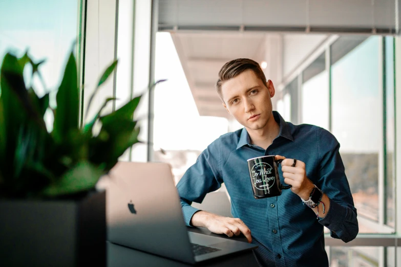 man in blue shirt sitting on laptop computer with coffee