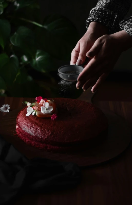 someone putting flowers on a red cake on a table