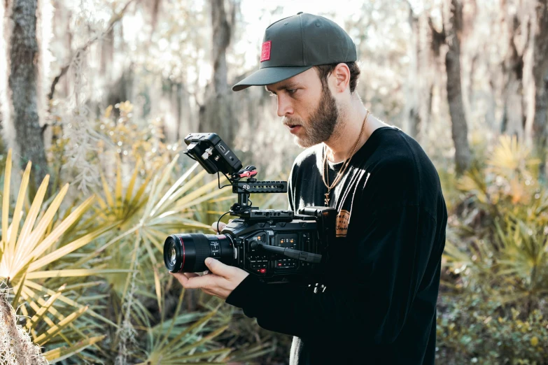 the man is filming outside near the trees