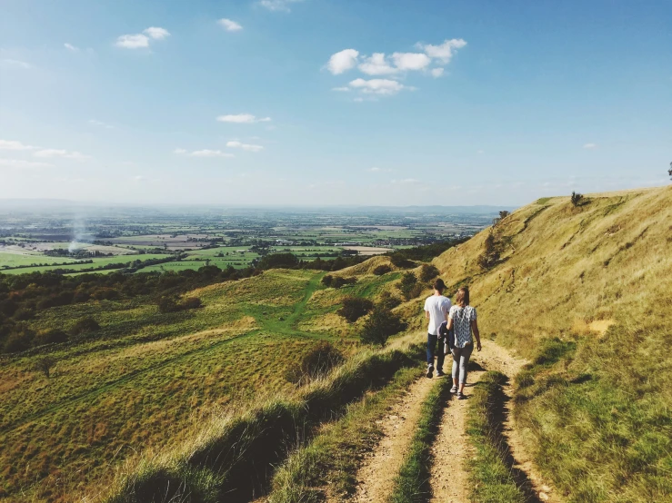 two people walking up a hill near some grass