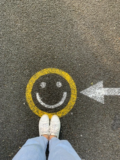 a persons legs standing next to a street with a smile drawn on it