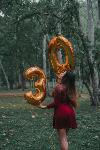 a woman in a red dress is holding gold balloons while the number 30 is being lifted above her head