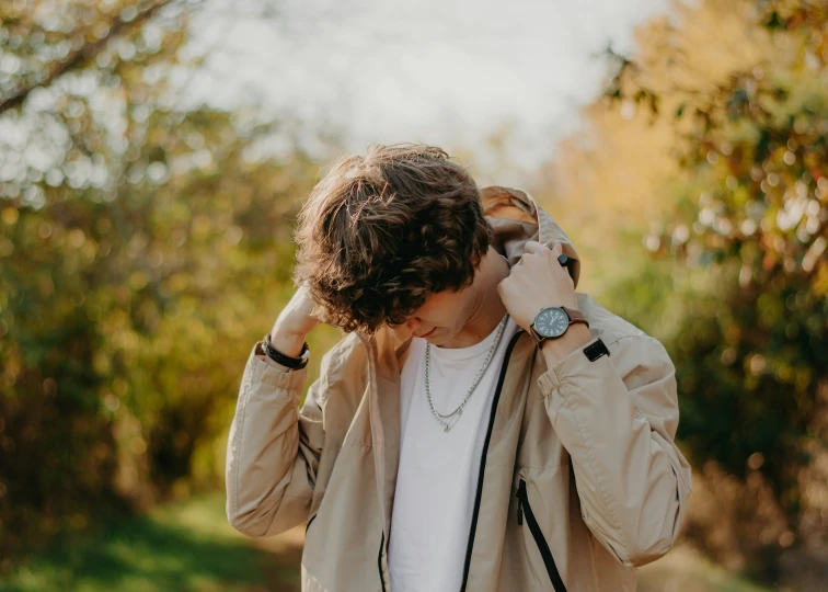 a young man covers his face with his hands while he walks through the woods