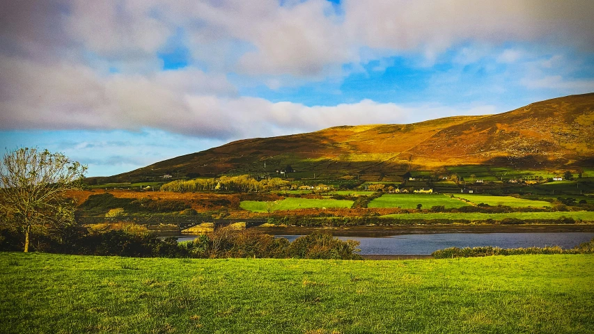 a grassy area with a body of water below it and a mountain in the distance