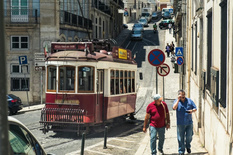 two men walk on the side of the street as a cable car drives down the street