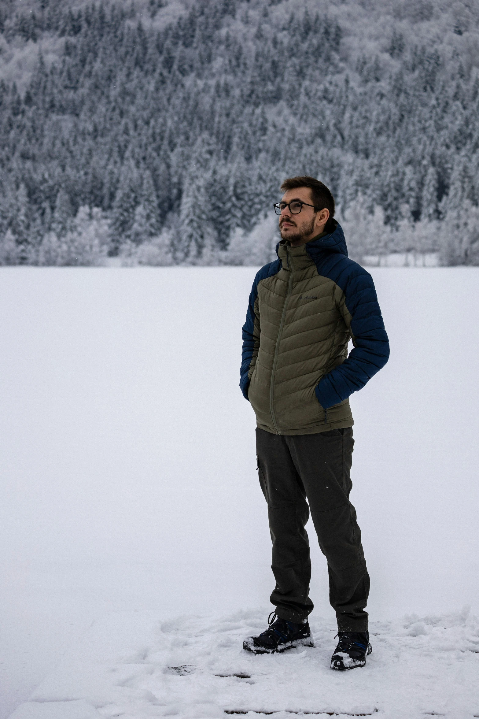 a man standing in the snow next to a forest