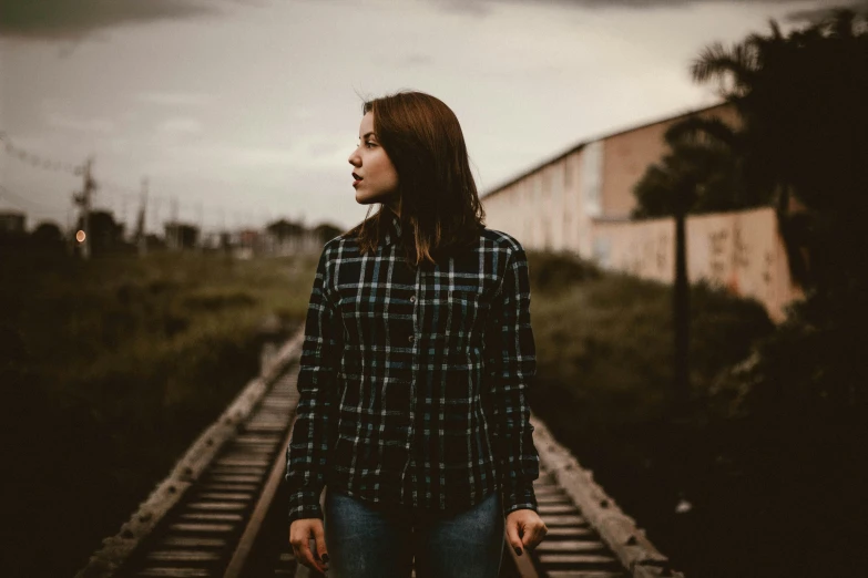 young woman walking down railroad tracks at dusk