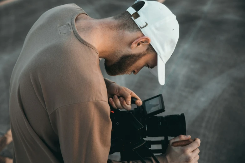 a man wearing a white hat taking a po on a video camera