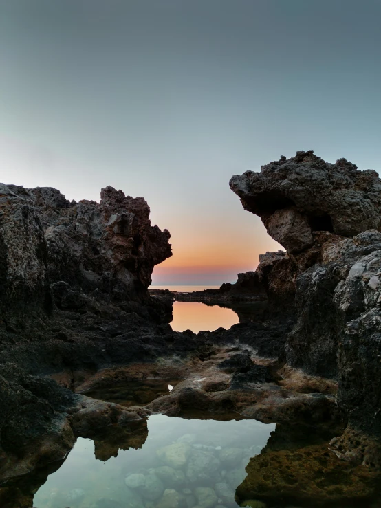 a large rock formation with the sun peeking out over it