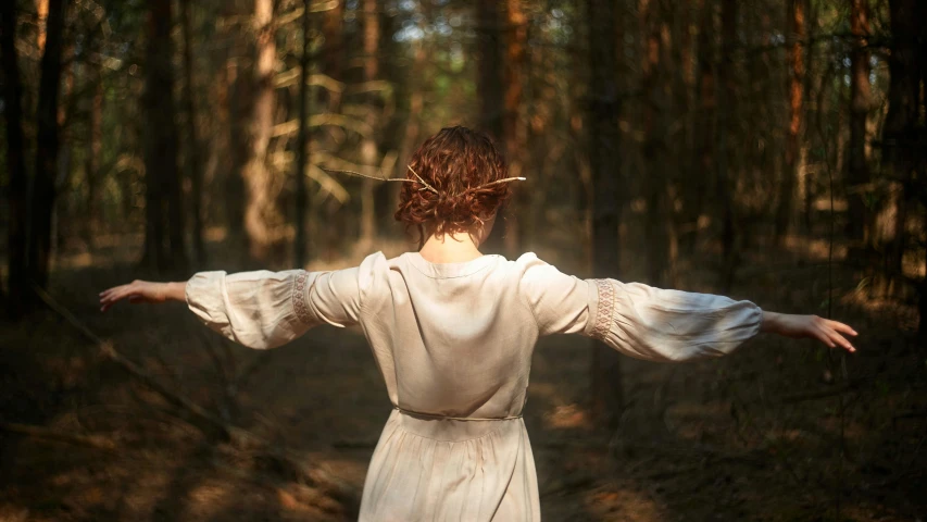 a woman is standing in a wooded area holding her arms out