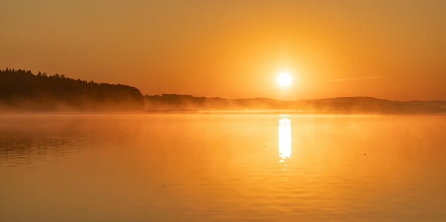 a sunset is reflected in the water as a boat sails through the mist