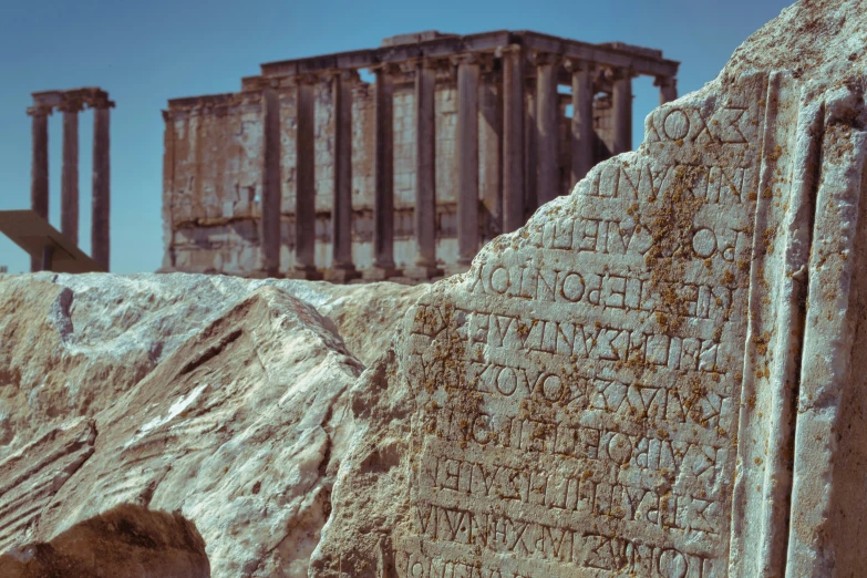 a rock with ancient writing in front of some ruins