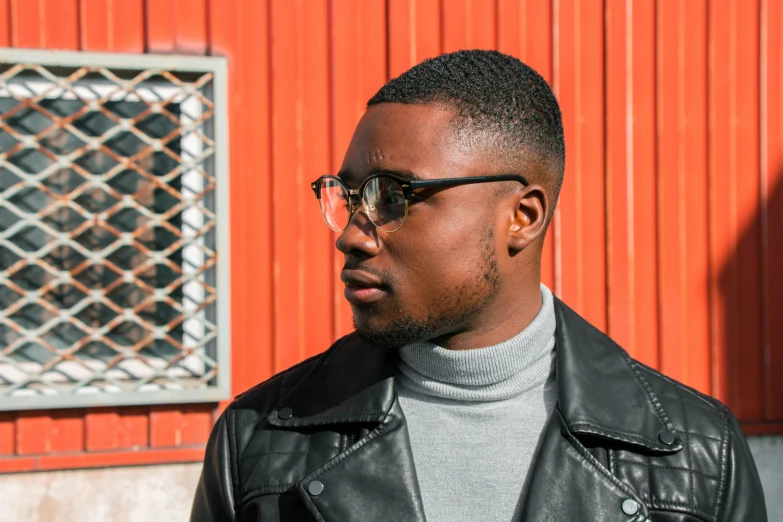 a man with glasses standing in front of a orange building