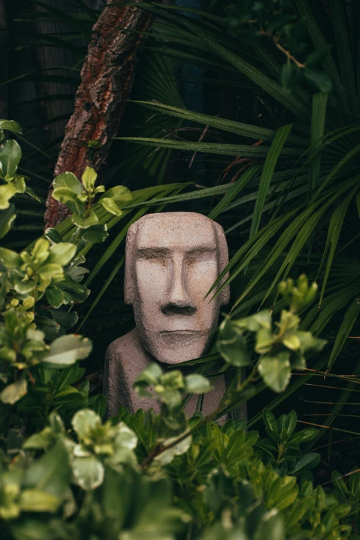 a white statue surrounded by green plants next to a tree