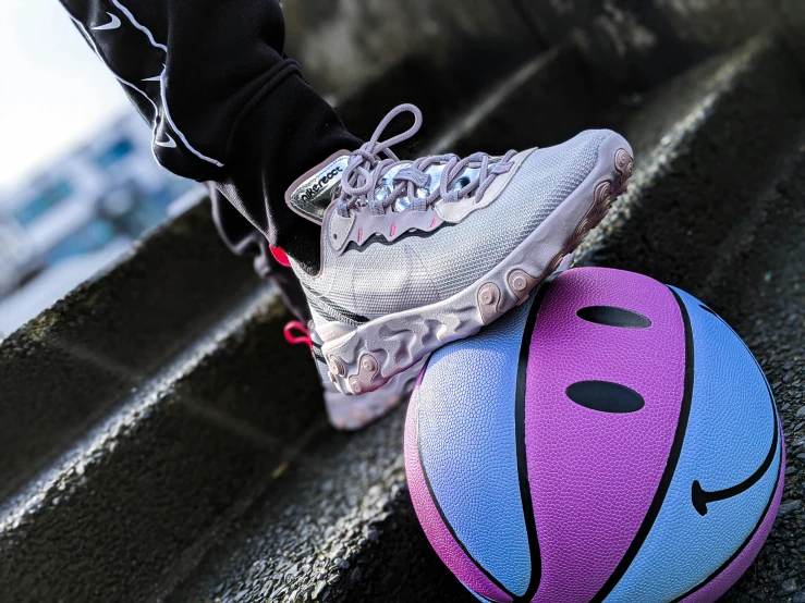 a person with gray and black shoes and grey and pink running shoe next to a purple and blue ball