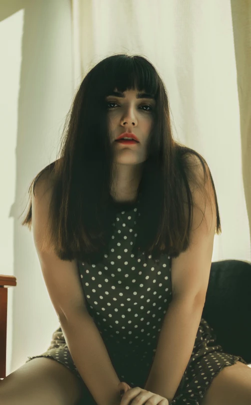 a woman with a white polka dot dress is sitting on a chair