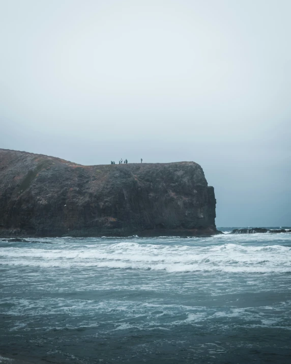 the people are on the top of a cliff at the ocean