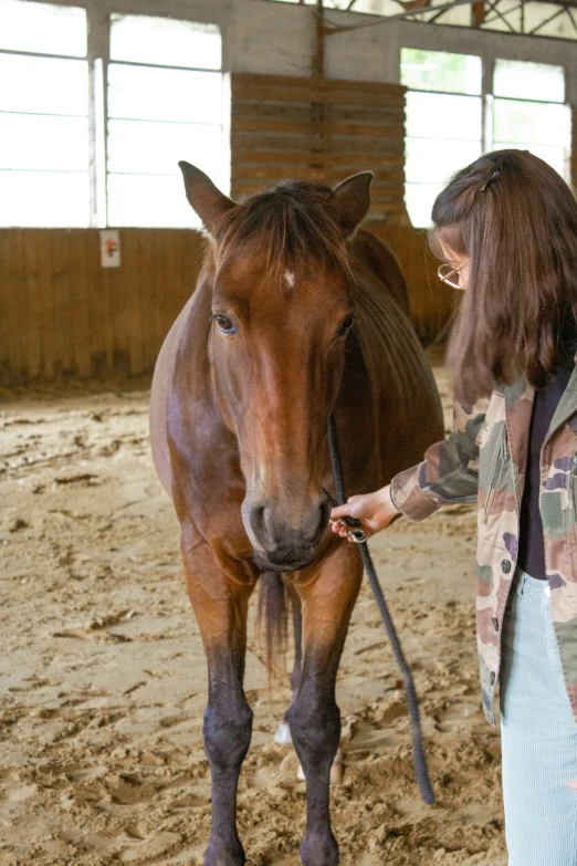 a woman in camouflage jacket standing next to a horse