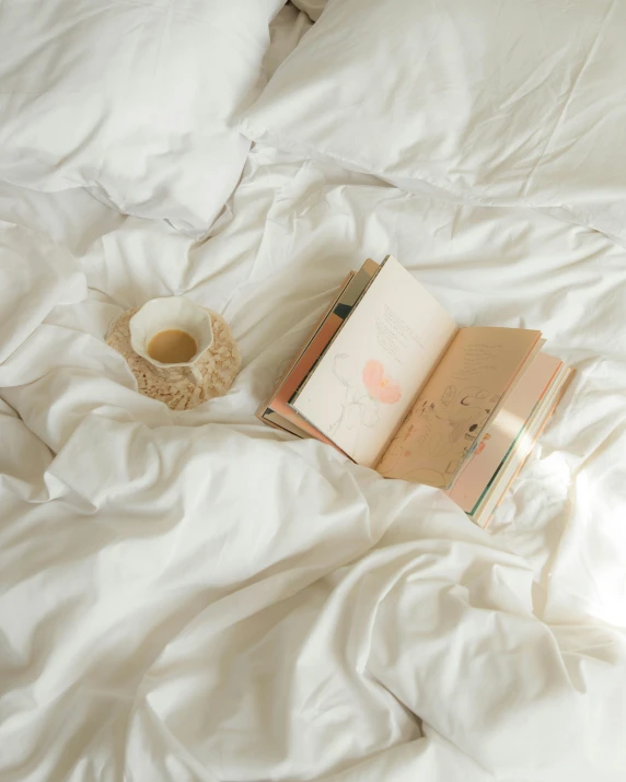 there is a small cup of coffee and a book on a bed