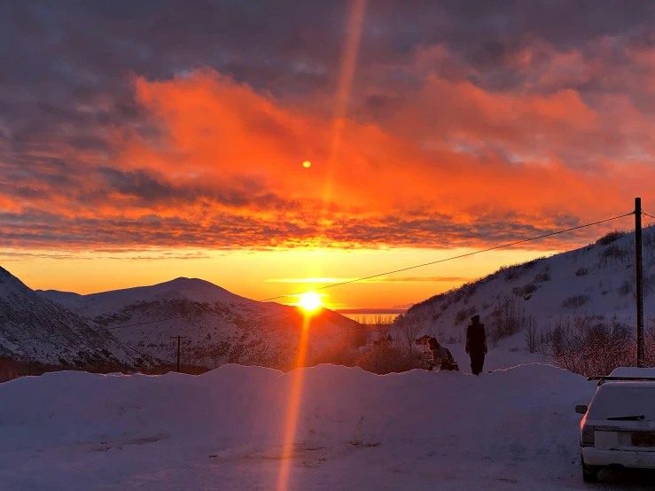 an orange sun shining over a mountain with two skiers