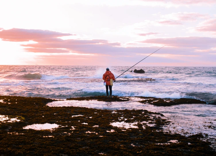 a man standing on rocks fishing near the ocean