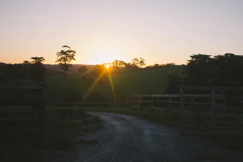 the sun is rising over a country dirt road