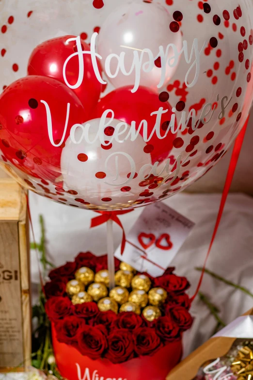 red heart shaped vase with balloons and a small gift box on table