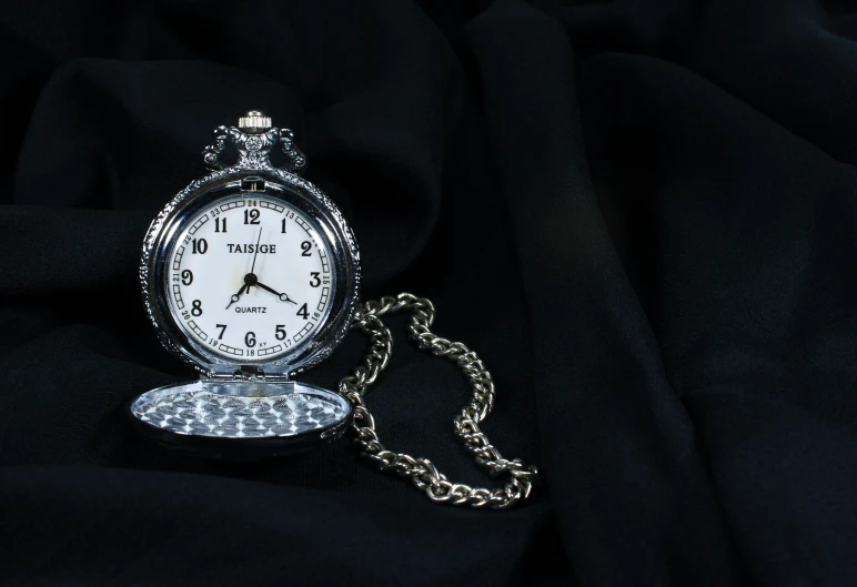 a white pocket watch sitting on a black blanket