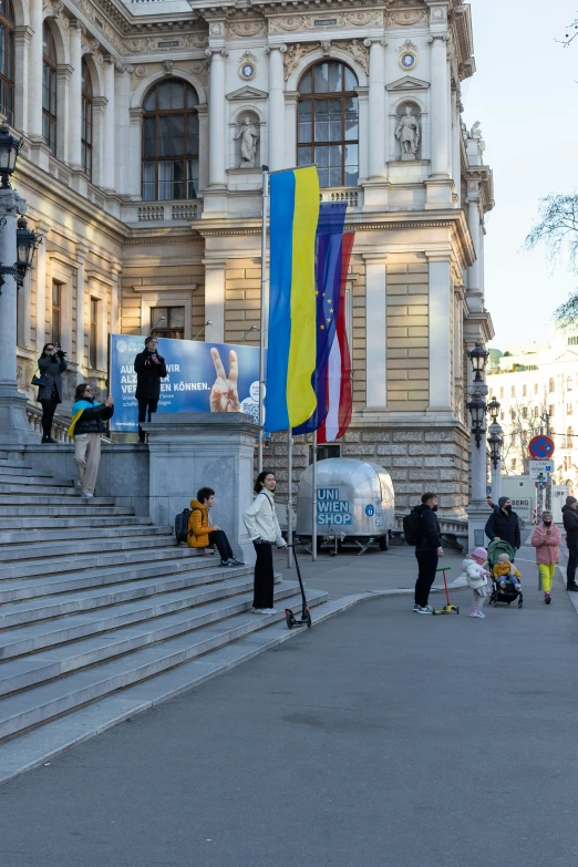 several people sitting on the steps of a building with a colorful flag